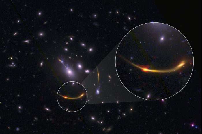 Imagen compuesta del cúmulo de galaxias MACSJ 0138 con datos del Atacama Large Millimeter/submillimeter Array (ALMA) y del telescopio espacial Hubble de la NASA. La sección ampliada muestra un punto rojo anaranjado brillante que representa el polvo frío observado en frecuencias de radio usando ALMA. El polvo frío ayuda a los científicos a calcular indirectamente la cantidad de gas de hidrógeno (necesario par la formación de estrellas) presente en las galaxias del cúmulo. Créditos: ALMA (ESO/NAOJ/NRAO)/S. Dagnello (NRAO), STScI, K. Whitaker et al.