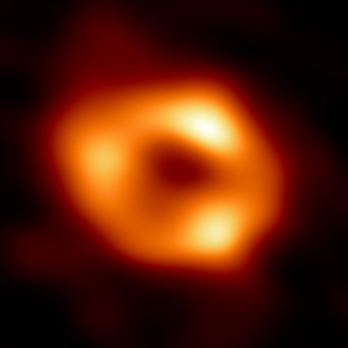 Esta es la primera imagen de Sagitario A* (Sgr A*), el objeto compacto supermasivo en el centro de nuestra galaxia, y constituye la primera prueba visual directa de la presencia de un agujero negro. Fue captada por el Event Horizon Telescope (EHT), una red de ocho radio observatorios distribuidos por todo el planeta para formar un único telescopio virtual del tamaño de la Tierra. El telescopio toma su nombre del "horizonte de eventos", es decir, el límite del agujero negro más allá del cual no puede escapar la luz. Aunque no podemos ver el horizonte de eventos en sí, porque no puede emitir luz, el gas resplandeciente que orbita alrededor del agujero negro tiene una clara signatura: una región central oscura (llamada "sombra") rodeada por una estructura brillante en forma de anillo. La nueva imagen capta la luz curvada por la poderosa gravedad del agujero negro, de cuatro millones de veces la masa de nuestro Sol. La imagen del agujero negro Sgr A* es un promedio de las diferentes imágenes que la Colaboración EHT ha extraído de sus observaciones de 2017. Créditos: Colaboración EHT