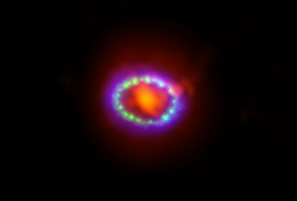 <p>Imagen compuesta de la supernova 1987A. Los datos recabados por ALMA (en rojo) muestran el polvo recién formado en el centro del material remanente. Los datos de HST (en verde) y Chandra (en azul) muestran la onda expansiva. Créditos: Alexandra Angelich (NRAO/AUI/NSF); NASA Hubble; NASA Chandra.</p>
