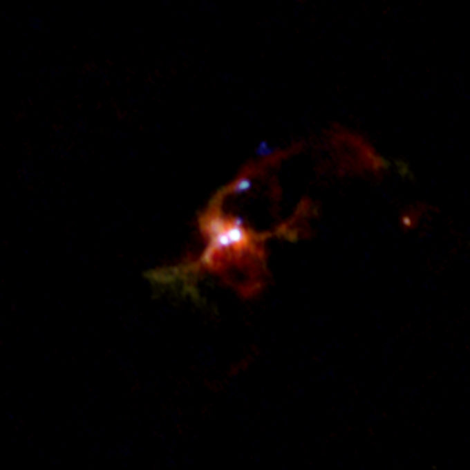 ALMA composite image of a massive binary protostar IRAS 16547-4247. Different colors show the different distributions of dust particles (yellow), methyl cyanide (CH3CN, red), salt (NaCl, green), and hot water vapor (H2O, blue). Dust and methyl cyanide are distributed widely around the binary, whereas salt and water vapor concentrate in the disk around each protostar. The jets from one of the protostars, seen as several dots in the above image, are shown in light blue. Credit: ALMA (ESO/NAOJ/NRAO), Tanaka et al.