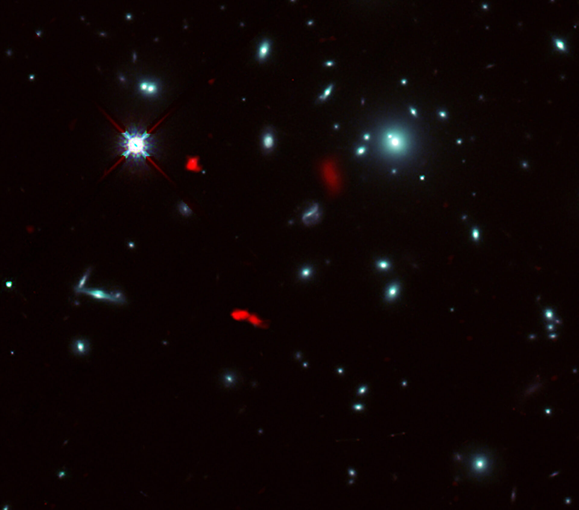 Imagen del cúmulo de galaxias RXCJ0600-2007 tomada por el telescopio espacial Hubble de la NASA/ESA combinada con imágenes de lente gravitacional de la lejana galaxia RXCJ0600-z6, situada a 12.400 millones de años luz de distancia, obtenidas con ALMA (en rojo). Debido al efecto de lente gravitacional producido por el cúmulo de galaxias, la imagen de RXCJ0600-z6 se vio intensificada y amplificada, y parece estar dividida al menos en tres partes. Créditos: ALMA (ESO/NAOJ/NRAO), Fujimoto et al., telescopio espacial Hubble de la NASA/ESA