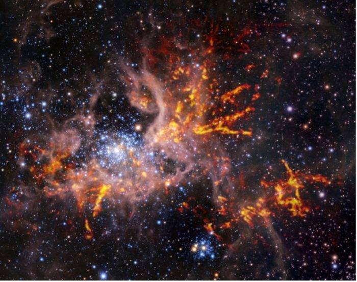 This composite image shows the star-forming region 30 Doradus, also known as the Tarantula Nebula. The background image, taken in the infrared, is itself a composite: it was captured by the HAWK-I instrument on ESO’s Very Large Telescope (VLT) and the Visible and Infrared Survey Telescope for Astronomy (VISTA), shows bright stars and light, pinkish clouds of hot gas. The bright red-yellow streaks that have been superimposed on the image come from radio observations taken by the Atacama Large Millimeter/submillimeter Array (ALMA), revealing regions of cold, dense gas which have the potential to collapse and form stars. The unique web-like structure of the gas clouds led astronomers to the nebula’s spidery nickname. Credit: ESO, ALMA (ESO/NAOJ/NRAO)/Wong et al., ESO/M.-R. Cioni/VISTA Magellanic Cloud survey. Acknowledgment: Cambridge Astronomical Survey Unit