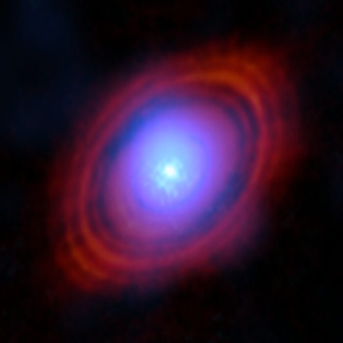 Astronomers have found water vapour in a disc around a young star exactly where planets may be forming. In this image, the new observations from the Atacama Large Millimeter/submillimeter Array (ALMA) show the water vapour in shades of blue. Near the centre of the disc, where the young star lives, the environment is hotter and the gas brighter. The red-hued rings are previous ALMA observations showing the distribution of dust around the star. Credit: ALMA (ESO/NAOJ/NRAO)/S. Facchini et al.